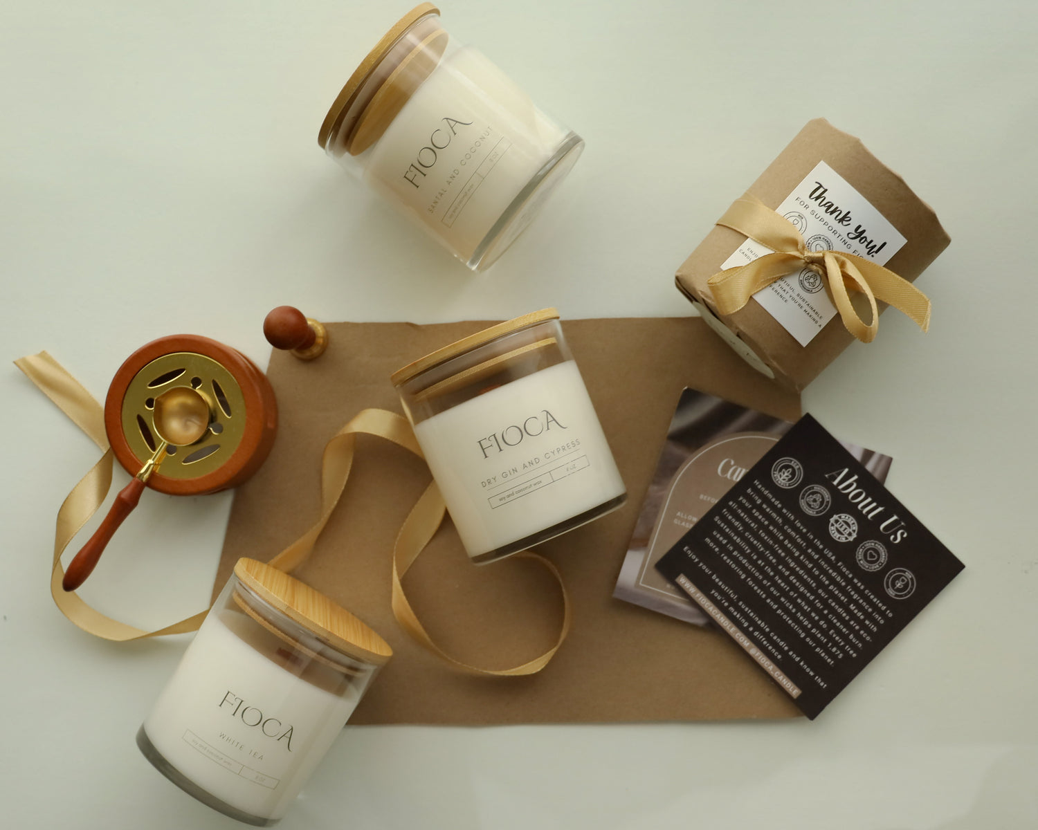 Flat lay of Fioca candles with kraft-wrapped gifts, a sealing stamp, and brand cards, showcasing the eco-friendly packaging and elegant presentation