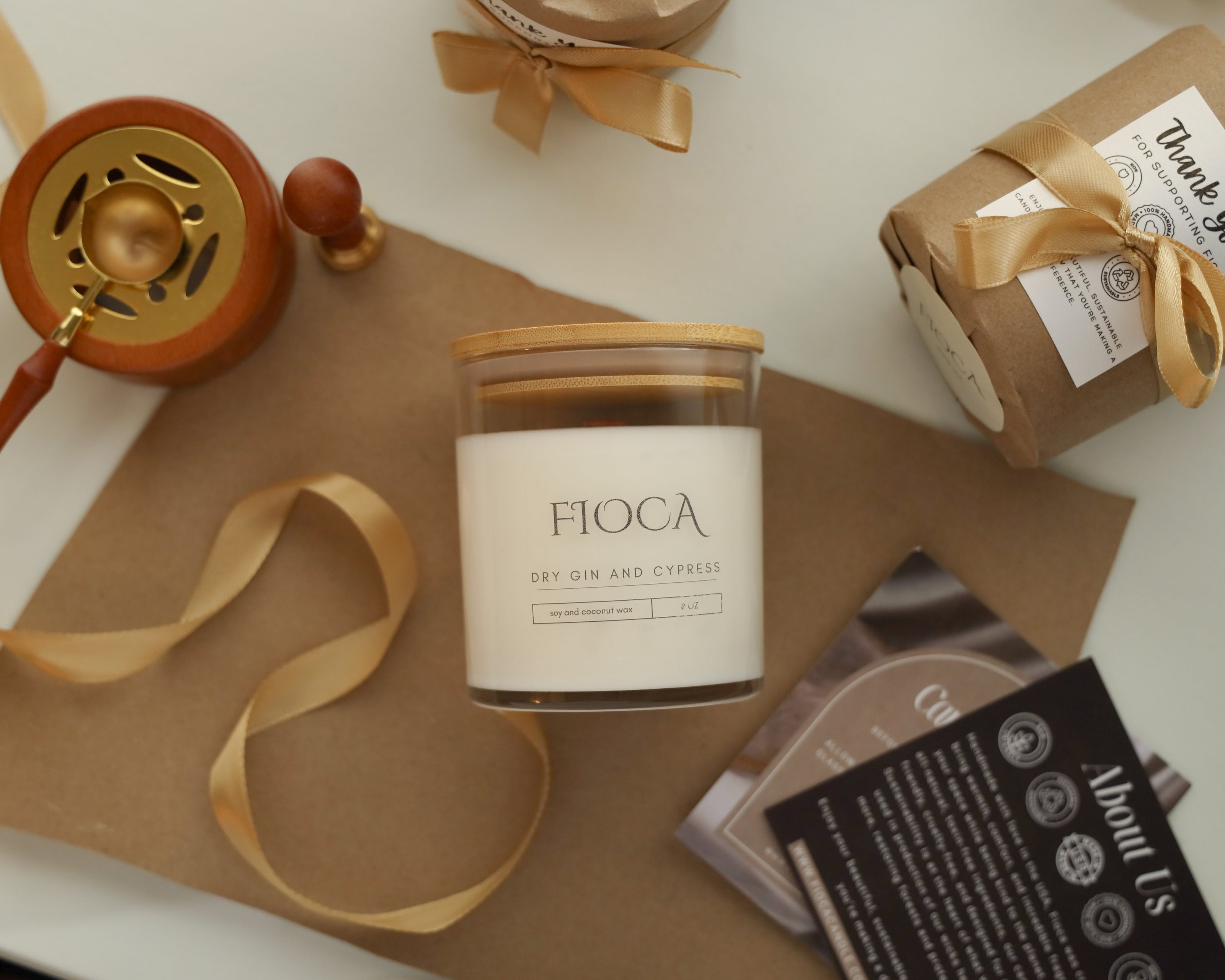 Fioca Dry Gin and Cypress candle displayed on kraft paper with gold ribbon and packaging, evoking a sense of handcrafted warmth and luxury