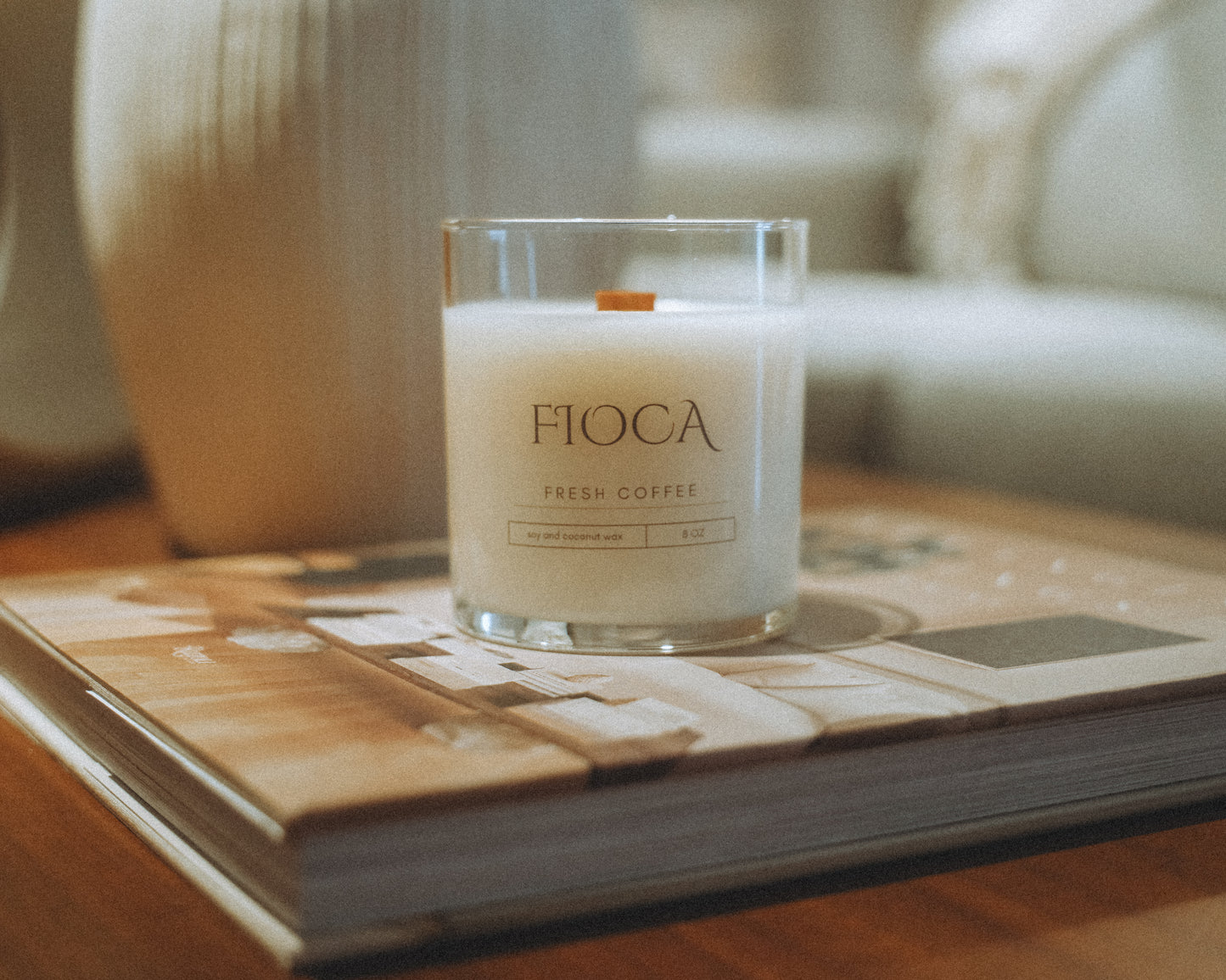 Fioca Fresh Coffee candle placed on a coffee table book, creating a cozy, serene ambiance with natural tones and soft light