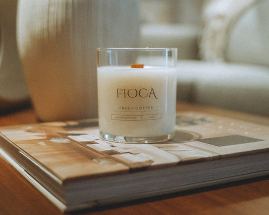 Fioca Fresh Coffee candle placed on a coffee table book, creating a cozy, serene ambiance with natural tones and soft light